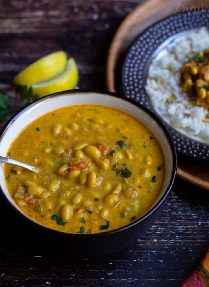 soy bean curry in a bowl with a spoon inside and with few lemon wedges and cilantro on the side