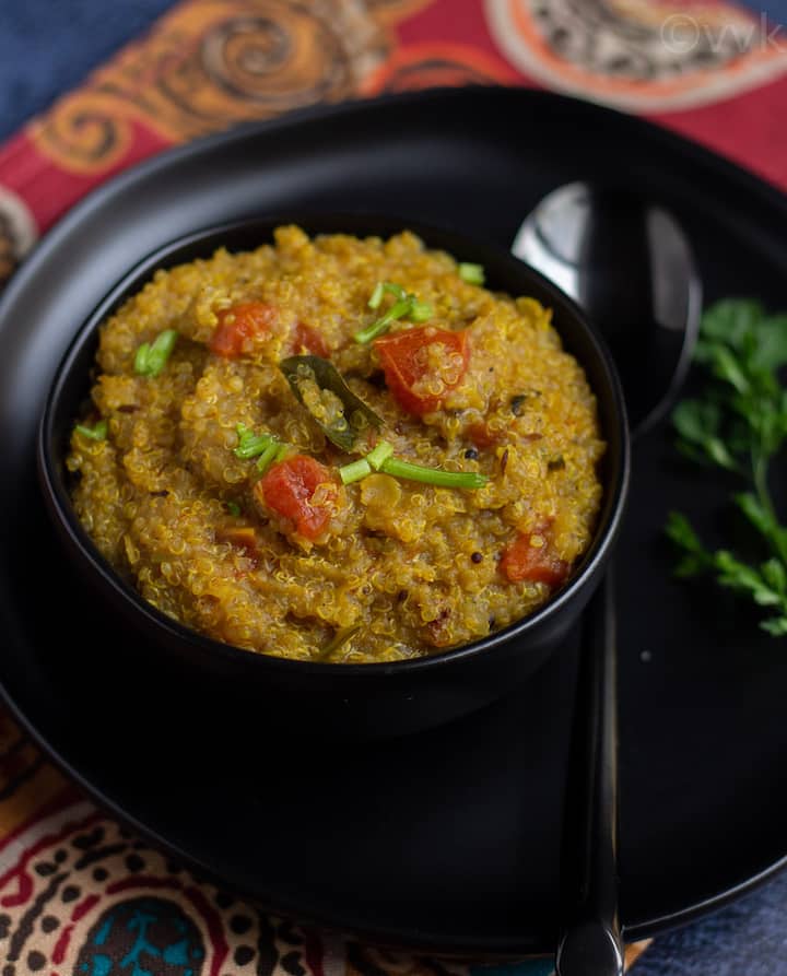 close up shot of instant pot quinoa rasam rice in a black bowl with a black spoon on the side