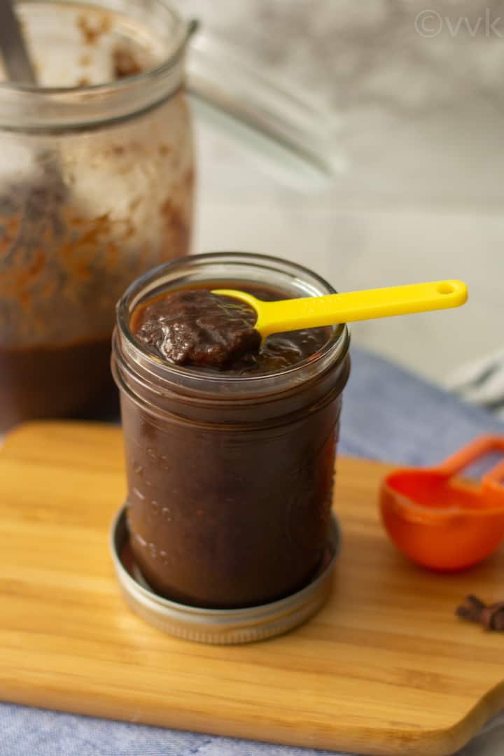 homemade tamarind paste in a glass jar placed on a wooden board with yellow spoon on top