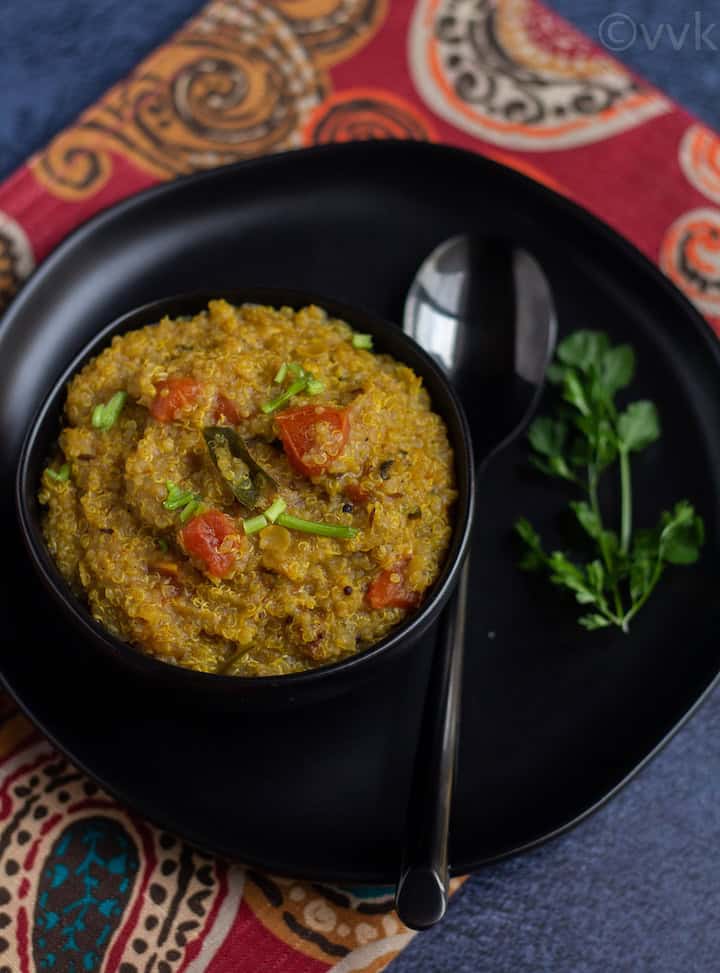 quinoa rasam rice on a black bowl placed on a black plate on a red fabric