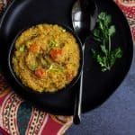 one pot rasam rice place on a black bowl with cilantro and a spoon on the side