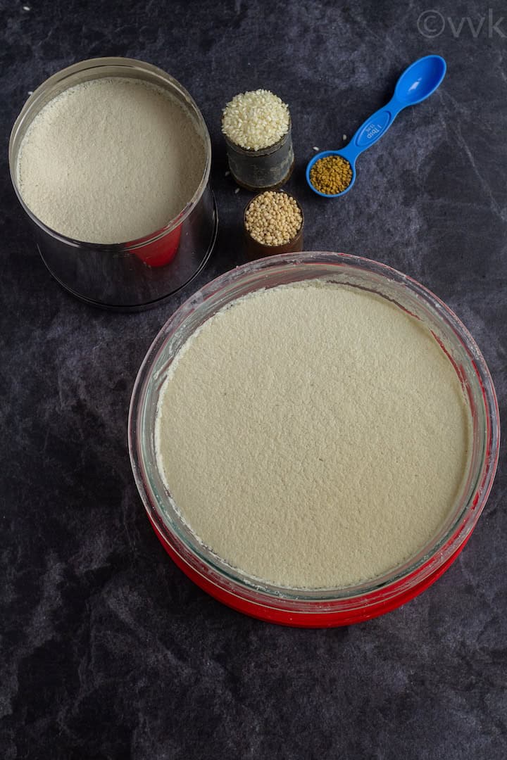 top angle shot of fermented idli dosa batter in two vessels with idli rice, urad dal and methi on the side