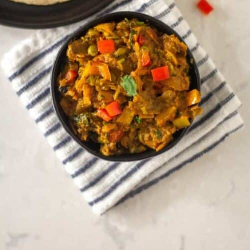 top angle square image of indian eggplant curry placed served in a black bowl