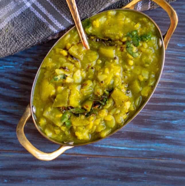 top angle shot of ridge gourd curry in a brass serve ware with a spoon inside