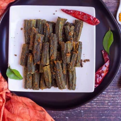 stuffed okra place on a white plate with dried red chilies on the side