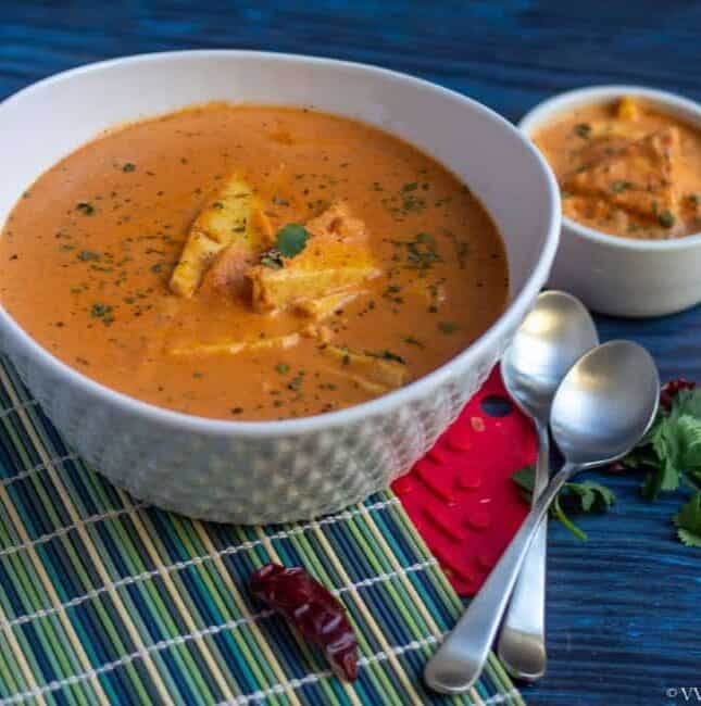 paneer butter masala in a white cermaic bowl with spoons on the side
