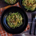 close up shot of zucchini noodles in a stacked black plate placed on a orange napkin