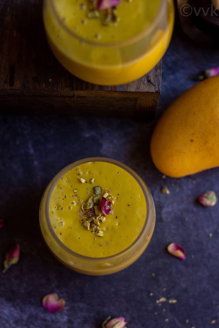 overhead shot of vegan mango lassi with rose petals and mangoes on the side