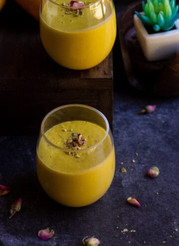 square image of mango lassi in two jars with a artificial succulent on the back as a prop