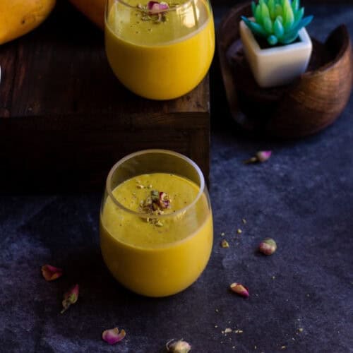 square image of mango lassi in two jars with a artificial succulent on the back as a prop