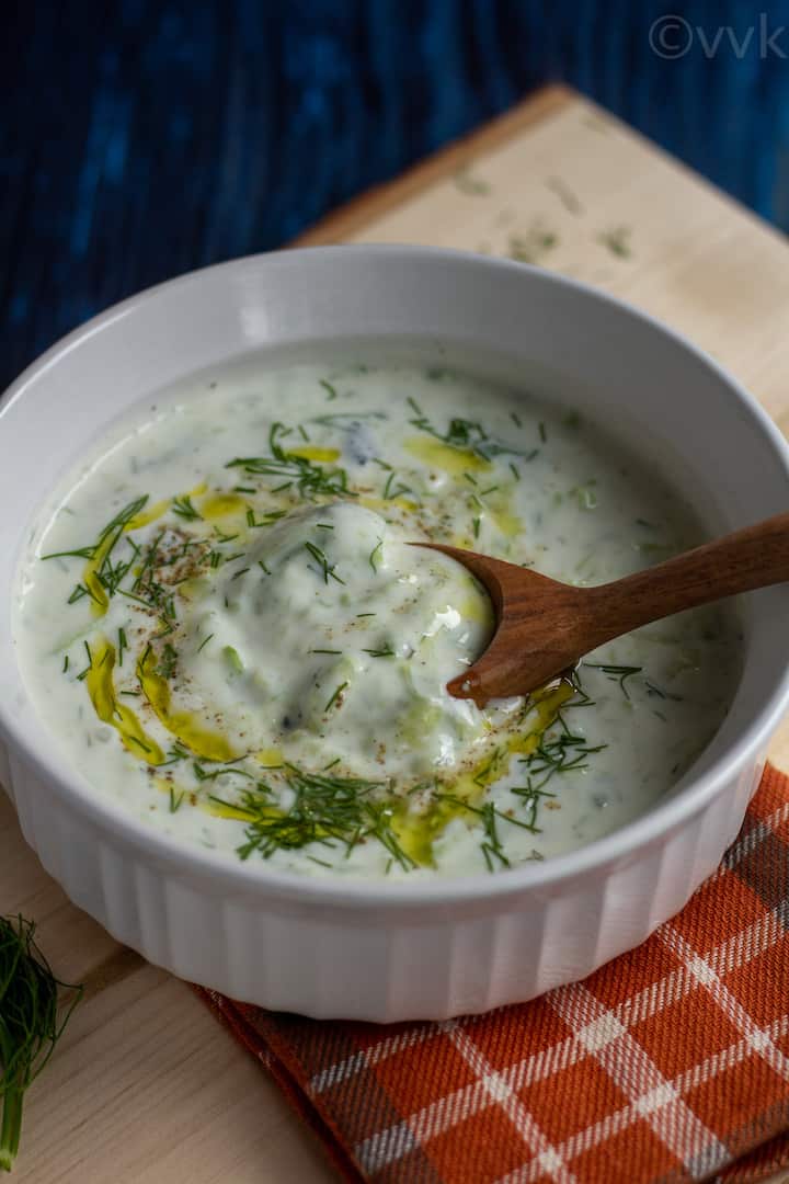 creamy greek cucumber and yogurt sauce in a white bowl with a wooden spoon placed inside
