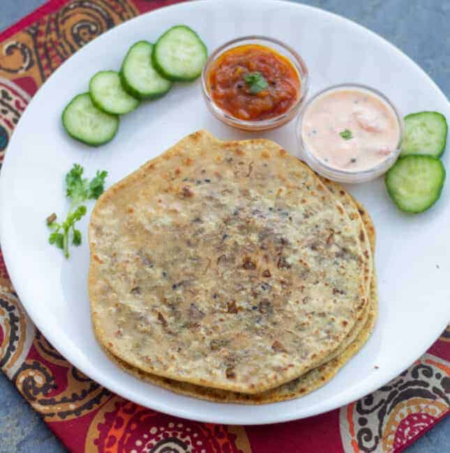 square image of brussels srouts stuffed paratha in white plate with raita and relish