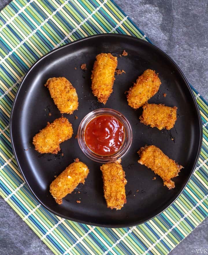 eggless fried cheese bites placed on a black plate with ketchup in the center