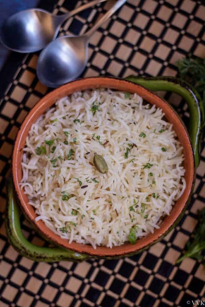 overhead shot of jeera rice placed on a striped mat with spoons on the side