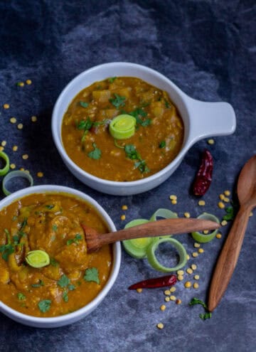 square image of leeks sambar in white bowls with wooden spoon on the side