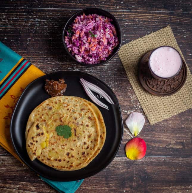 overhead shot of paratha platter with aloo paratha, lemon pickle, coleslaw and lassi