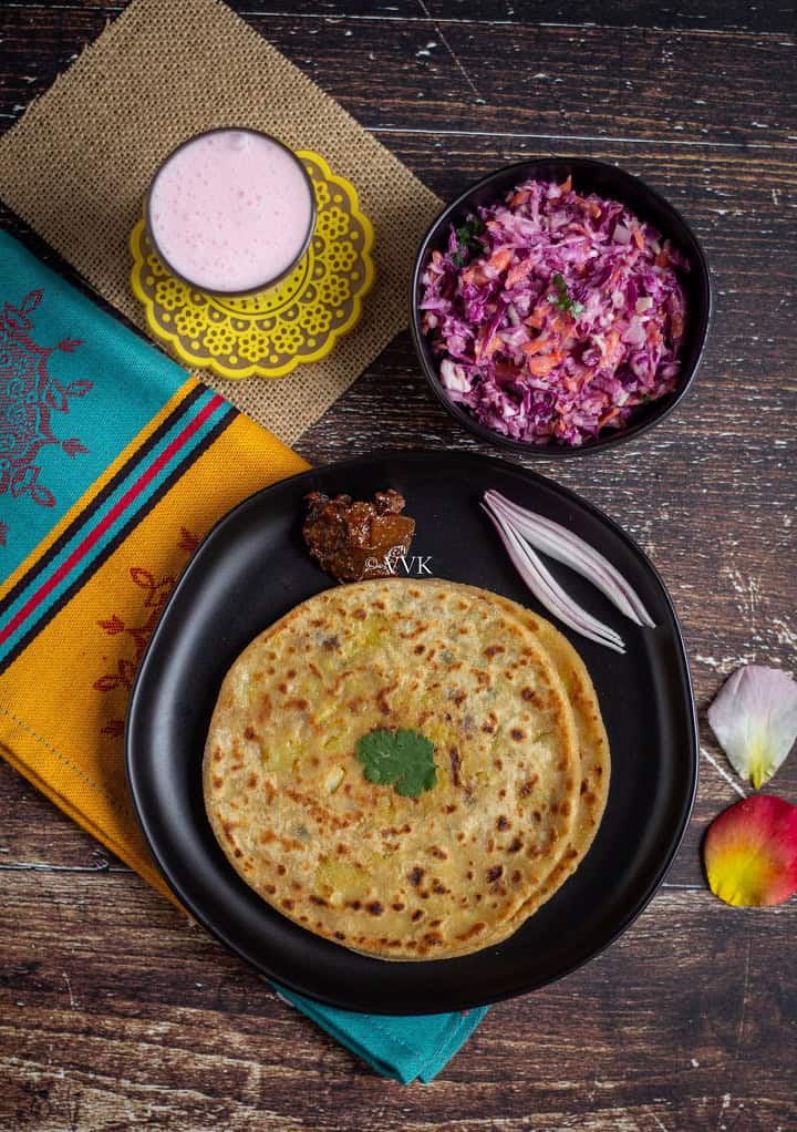 overhead length image shot of paratha thali with aloo paratha, lassi, salad and pickle