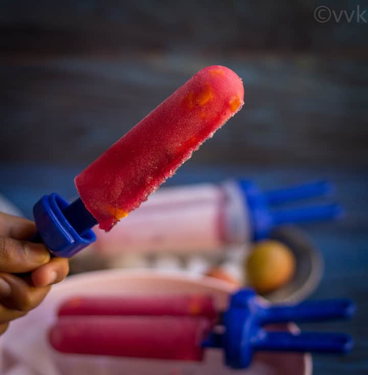 kid holding single black currant popsicle with mango and lychee