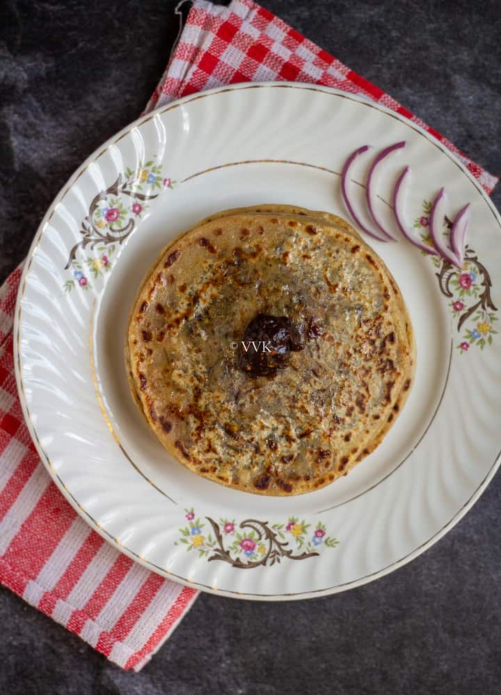cheese paratha with raisins chutney on top served in a white plate