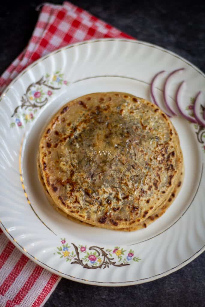 close up shot of cheese paratha in a white plate with onion slices on the side