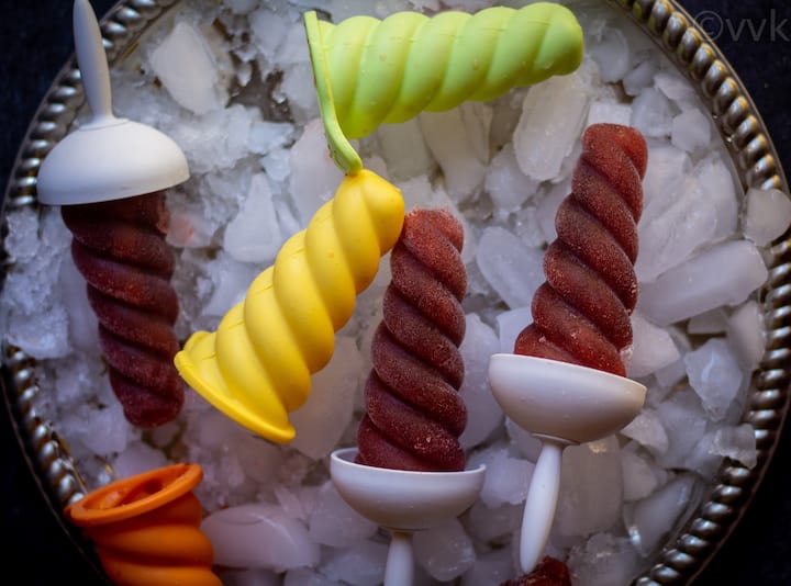 kala khatta popsicles placed on a plate with ice with molds on the side