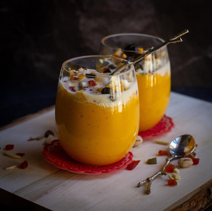 mango milkshake with spoon insde served on two tall glasses