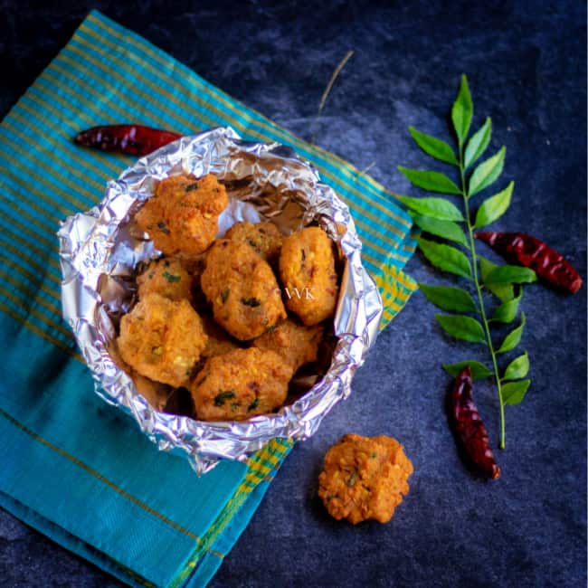 square image of paruppu vadai without onions blaced in a bowl with curryleaves on the side