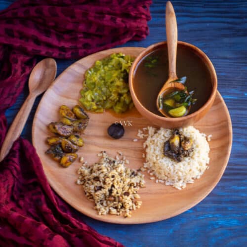 square image of pathiya sapadu with rice, milagu kuzhambu, kootu and rasam served on neem wood plate