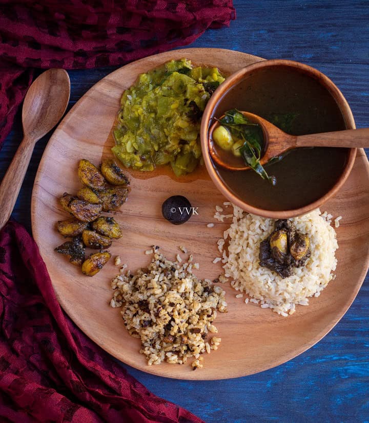 overhead shot of pathiya sapadu with rice, milagu kuzhambu, kootu and rasam served on neem wood plate