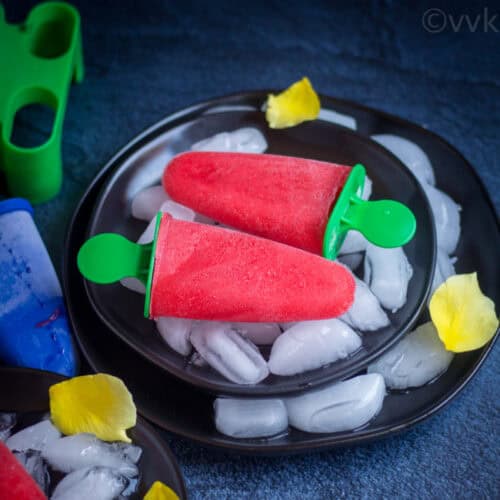 square image of rose syrup and rooh afza popsicle placed on a black plate with rose petals on the side