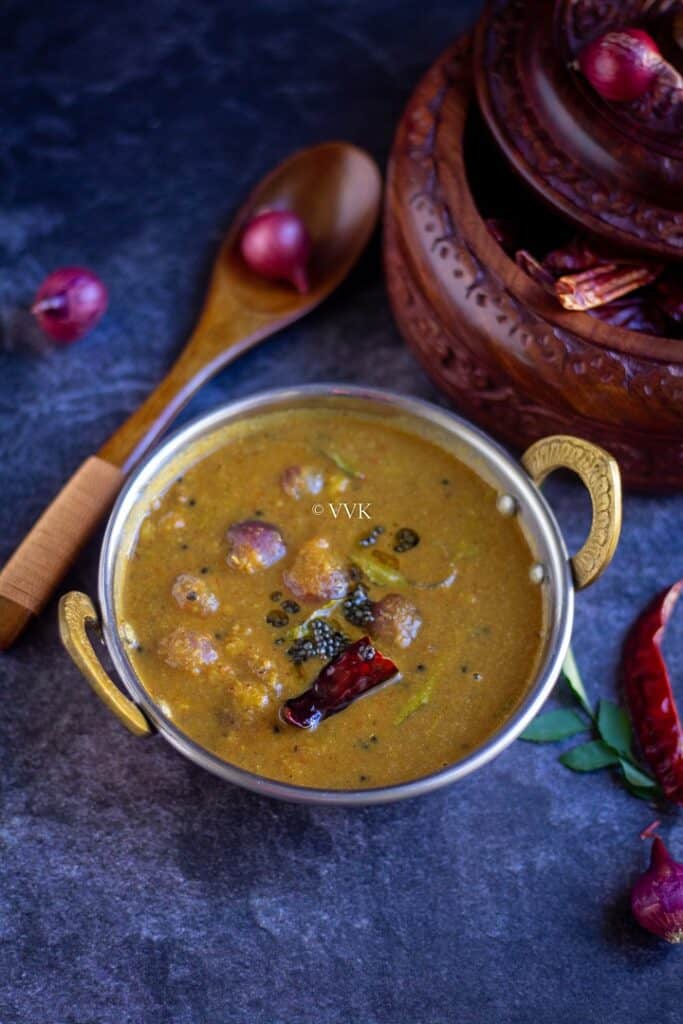arachuvitta sambar served in handi with shallots and curry leaves on the side