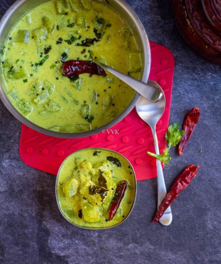 vellarikka pachadi served in steel serveware with spoons on the side and red chillies as a garnish