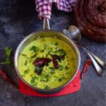 square image of vellarikka pachadi served in a steel sauce pan placed on a coaster and with spoons on the side