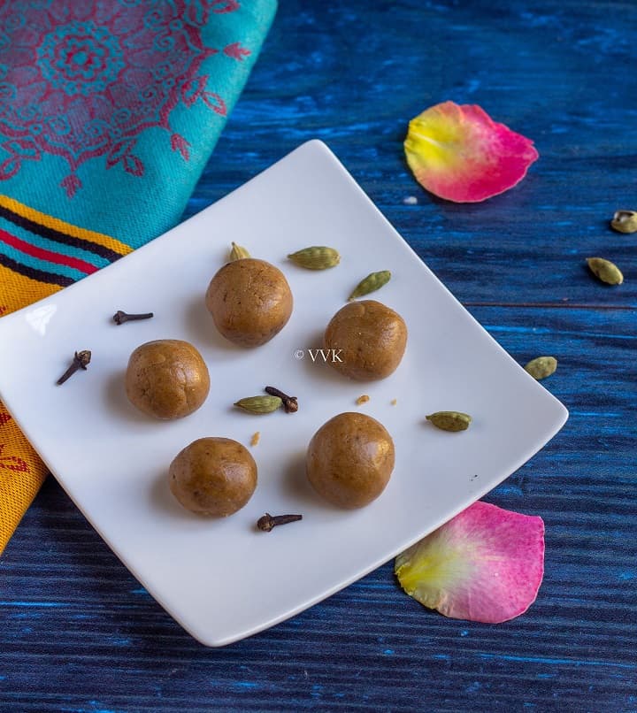 rice flour laddu in a white plate with cardamom and cloves and rose petals as garnish