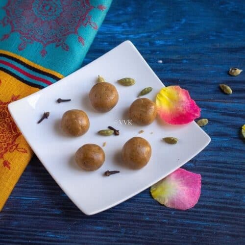 square image of akki unde in a white plate with cardamom and cloves and rose petals as garnish