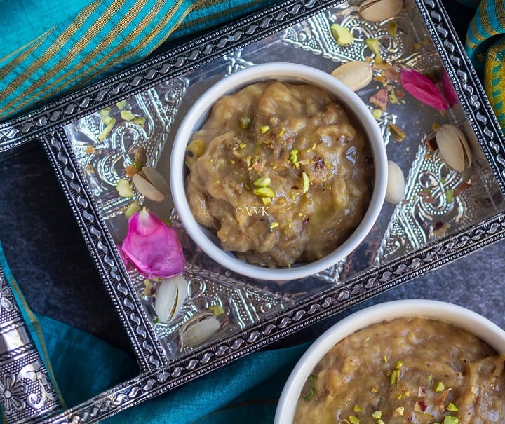 banana biscuit halwa served in a white bowl placed in a tray filled with nuts and rose petals