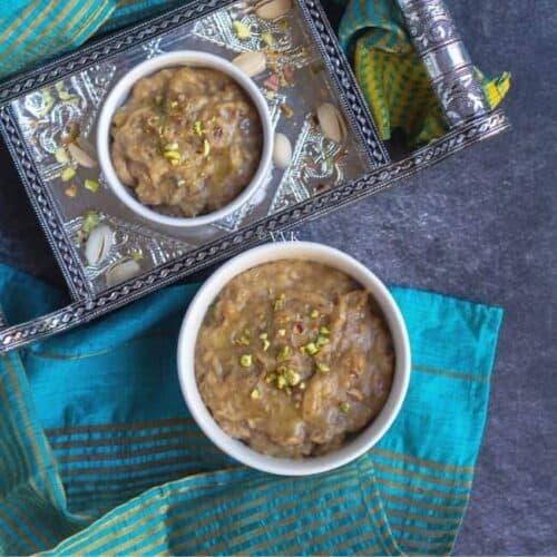 square image of banana biscuit halwa served in two white bowls with nuts on the side
