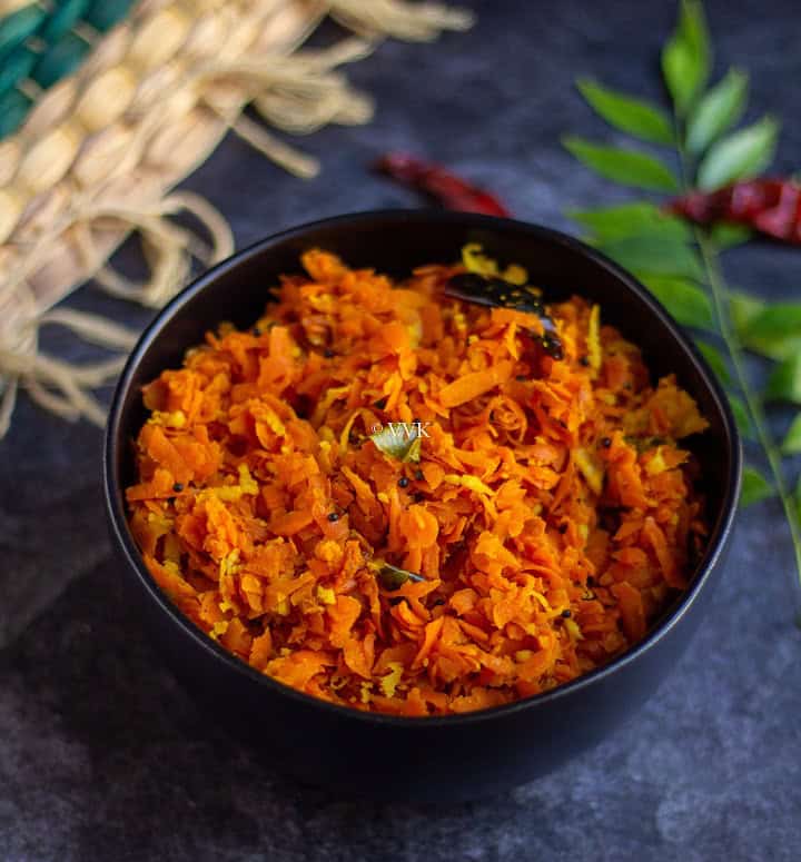 slanting shot of carrot stirfry in a black bowl with curry leaves on the side