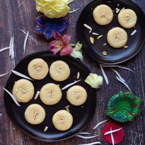 milk peda in two black plates sprinkled with white flowers all over