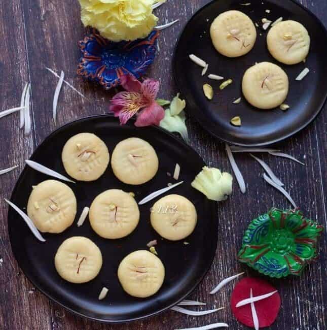 milk peda in two black plates sprinkled with white flowers all over
