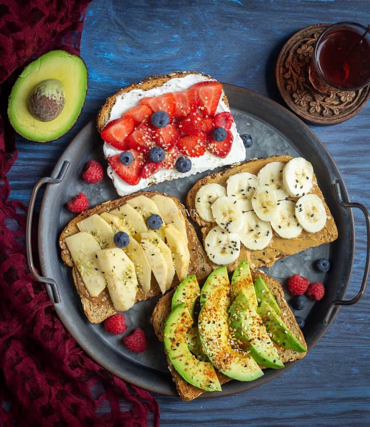 overhead shot of breakfast toast placed on a metallic tray with cut avocado and tea on the sides