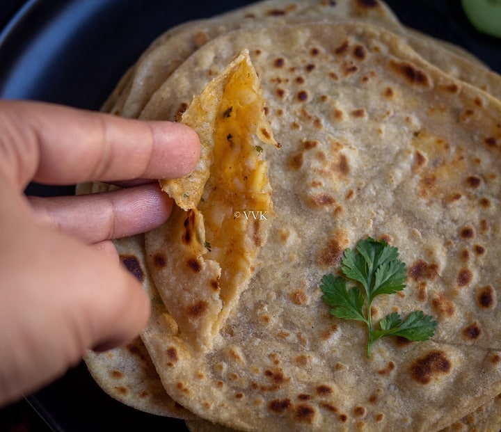 hand shot holding paneer paratha and showing the inside filling