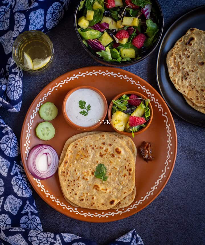 overhead shot of paneer paratha thali with raita, salad and pickle