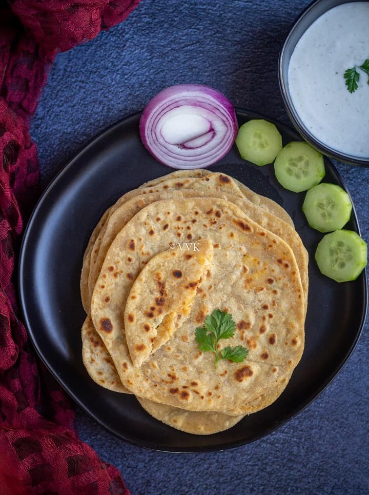 paneer paratha stacked on a black plate with a small piece on top