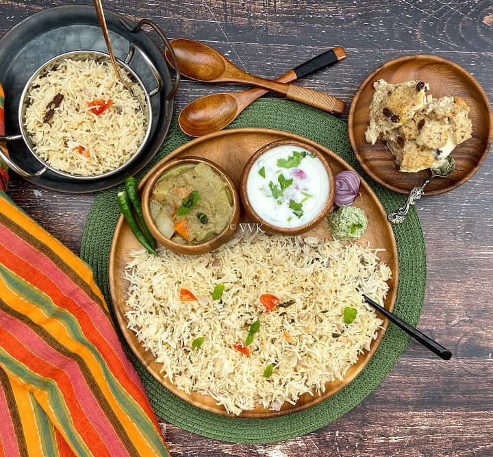 overhead shot of coconut milk pulao platter with assorted sides served on a wooden plate