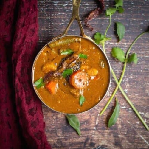 square image of thiruvathirai sambar with a maroon fabric on the side with some greens on the other side