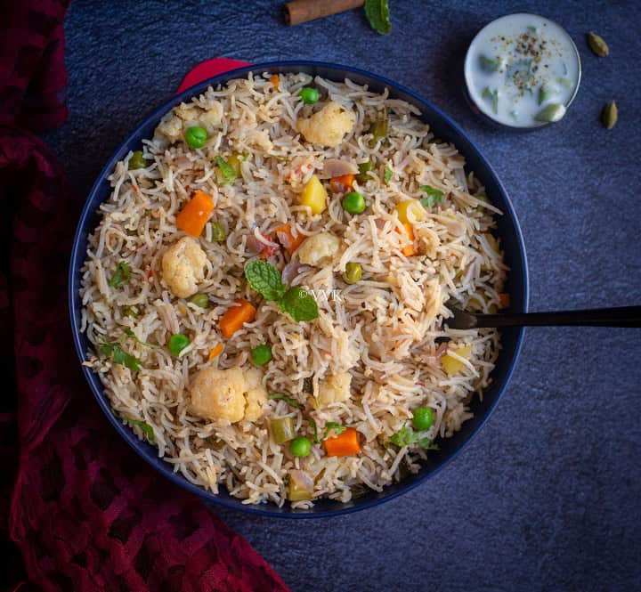 mixed vegetable pulao in blue bowl with a spoon inside served with raita