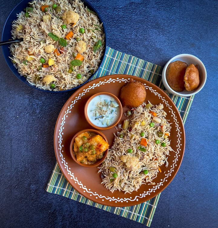 simple pulav platter with veg pulao, raita, matar paneer and bajji served in a terracotta plate