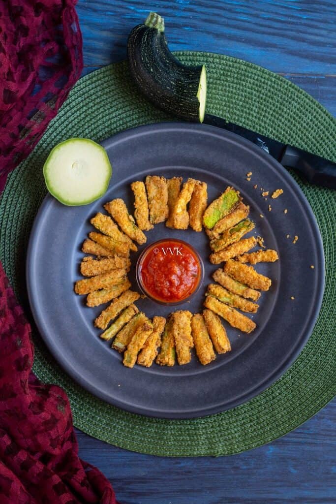 overhead shot of zucchini fries served on a rustic blue plate with marinara in the middle