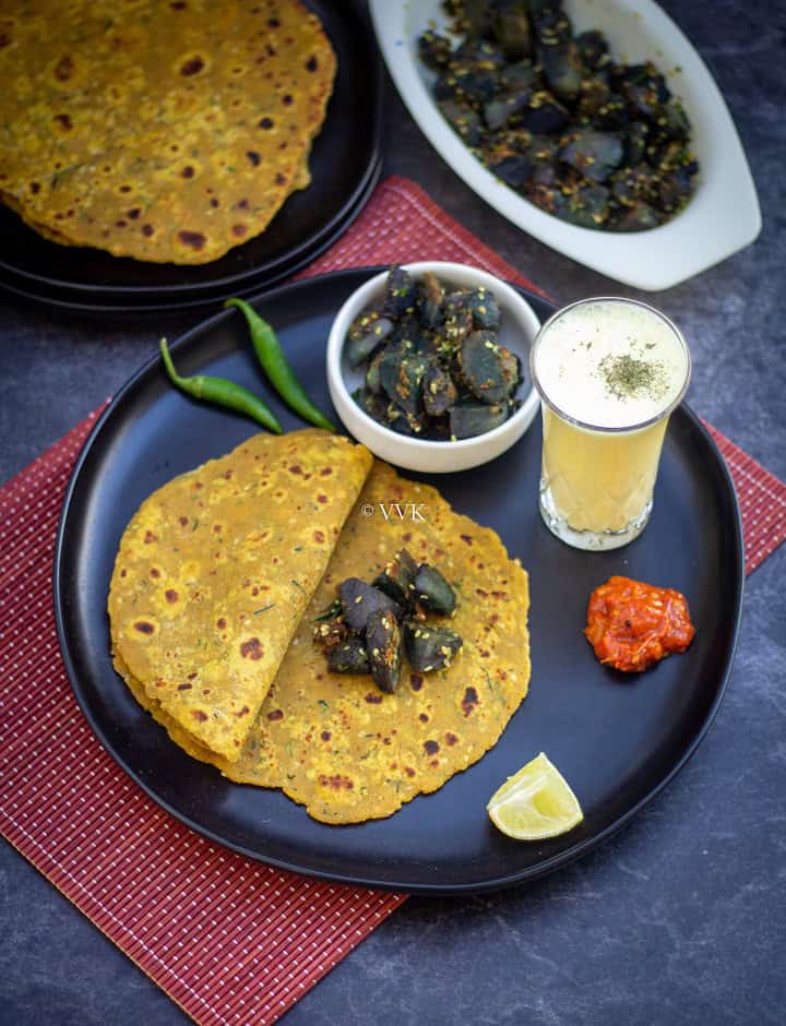 thepla lunch dinner menu with thepla, potato curry, pickle and buttermilk on a black plate placed on a red plate